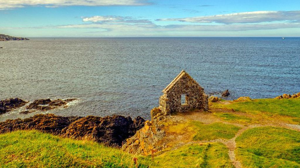 A stone building on a hill by the water.