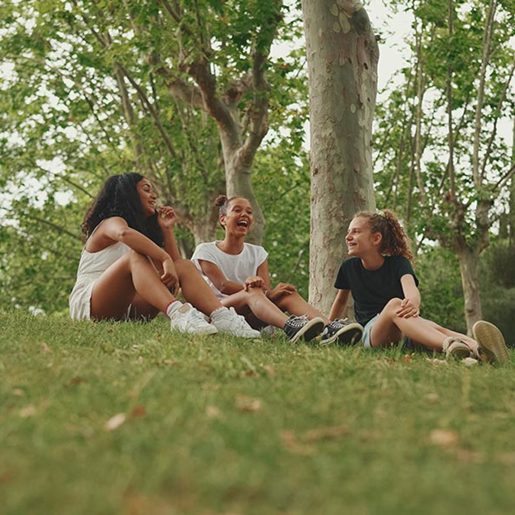 A group of women sitting on the grass by a tree.