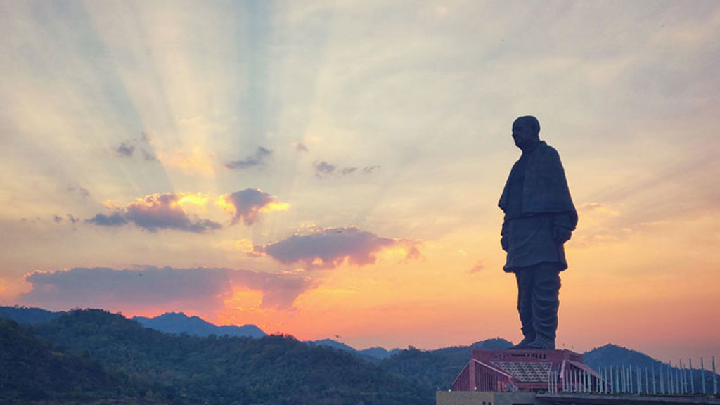 A statue of a person on a rock with a building and mountains in the background.