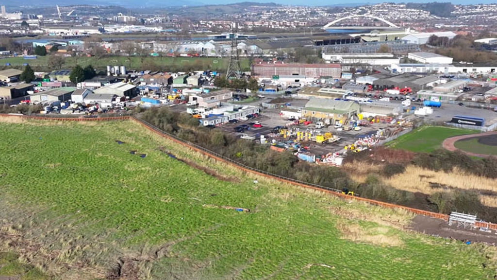 A large green field with buildings and trees in the background.
