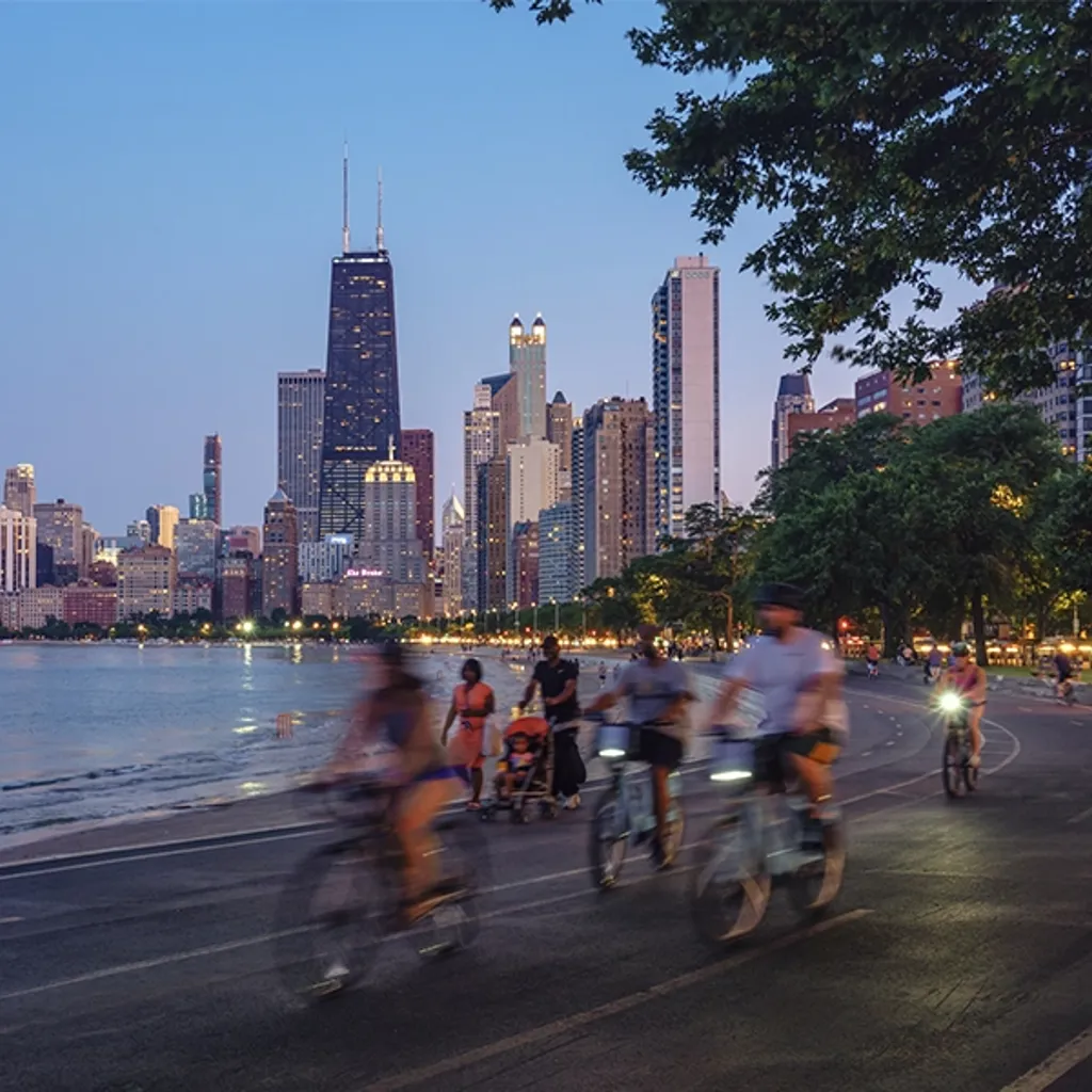 A group of people cycling on a street by a body of water in a city