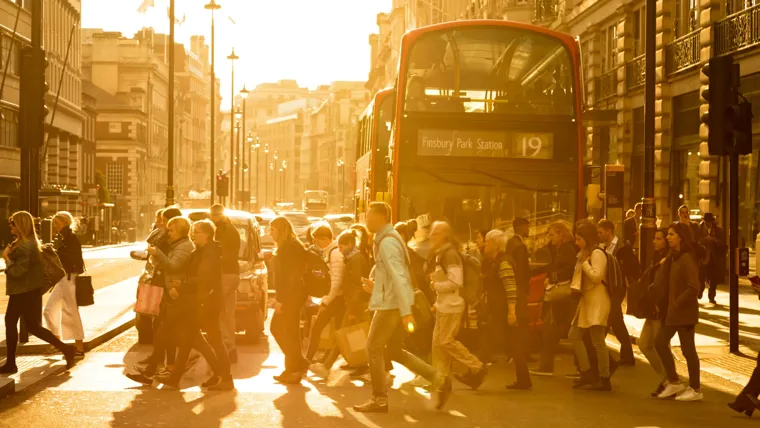 A group of people walking on a street next to a double decker bus.